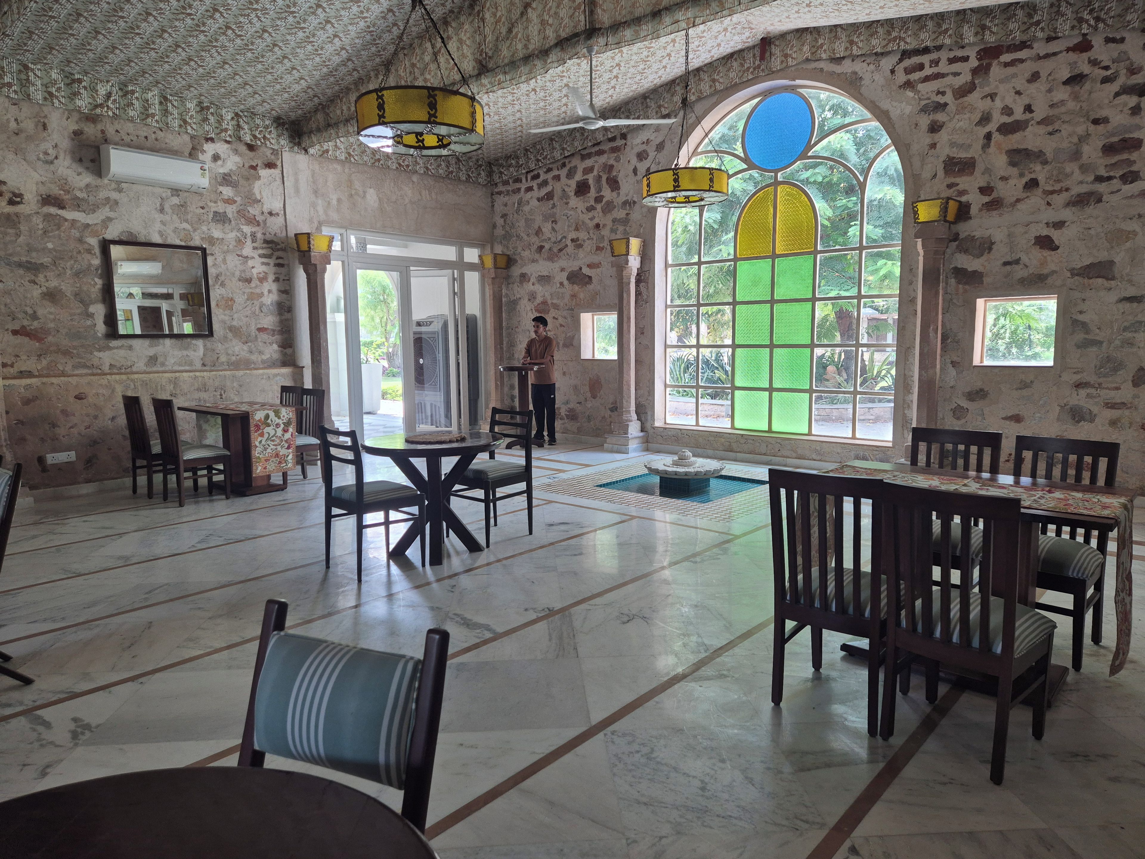 Una habitación espaciosa con paredes de piedra, ventanas grandes y una fuente.
