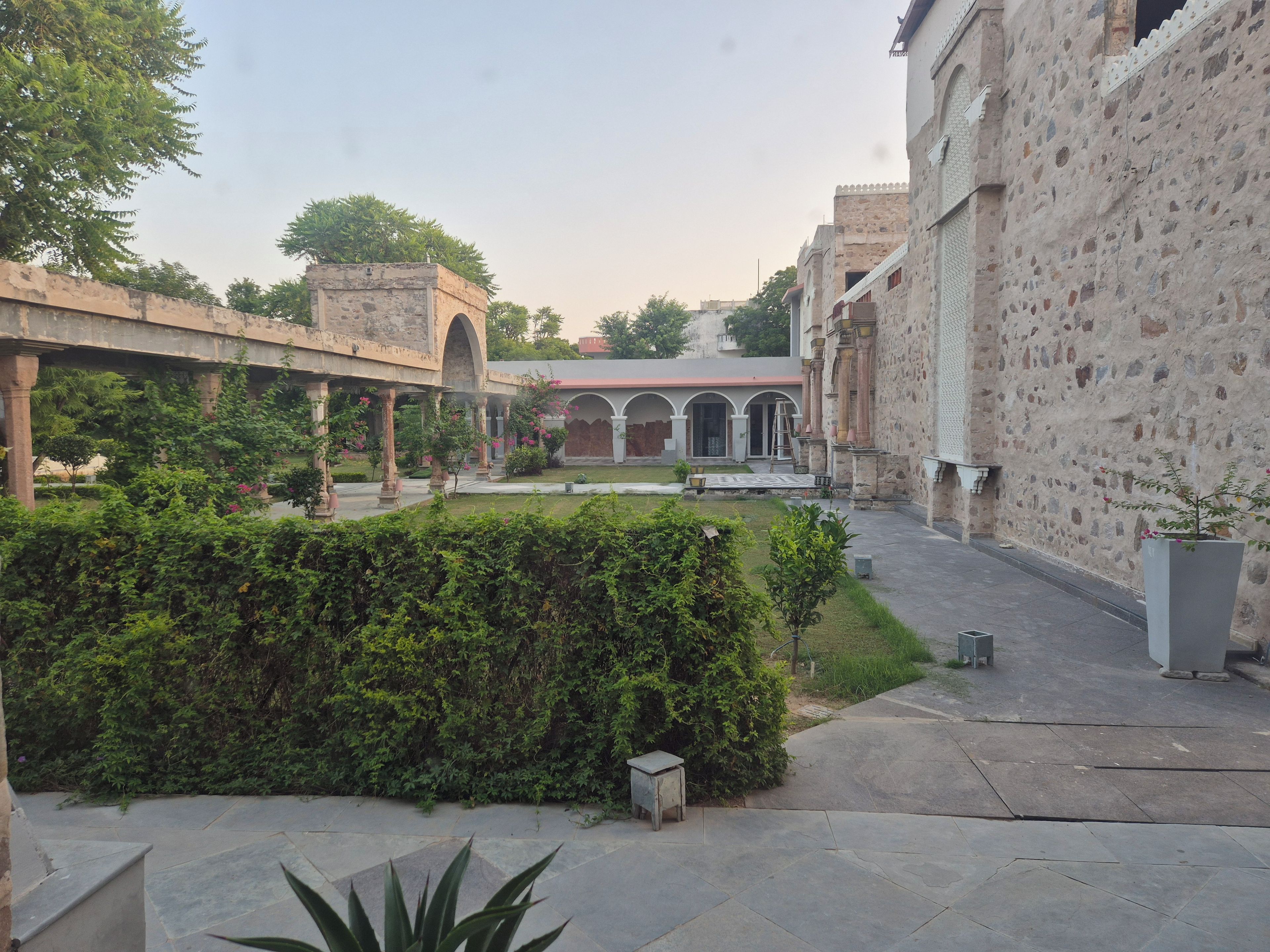 A courtyard with a stone wall, a covered walkway, and a building with arches.