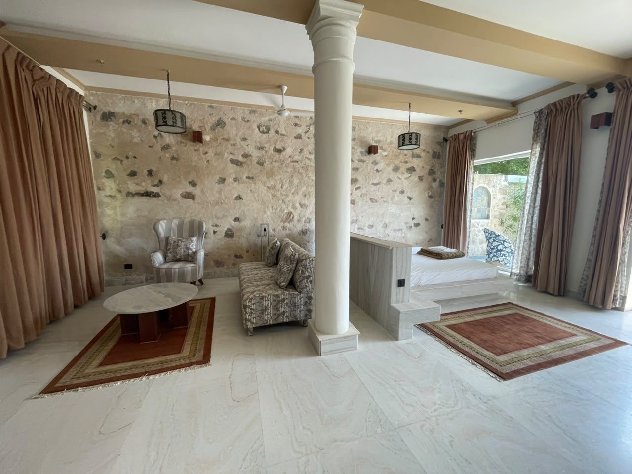 A spacious living area with a stone wall, a striped armchair, a patterned sofa, and a fireplace.