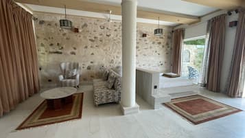 A spacious living area with a stone wall, a striped armchair, a patterned sofa, and a fireplace.
