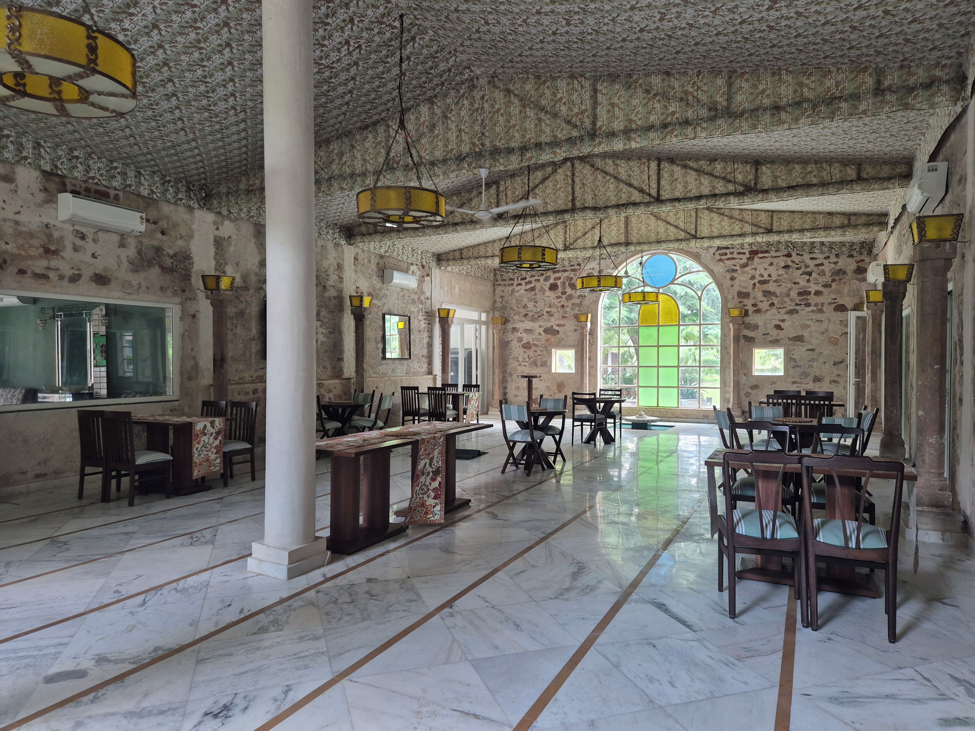 A spacious hall with marble flooring, stone walls, and multiple tables and chairs arranged for dining.
