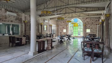 A spacious hall with marble flooring, stone walls, and multiple tables and chairs arranged for dining.