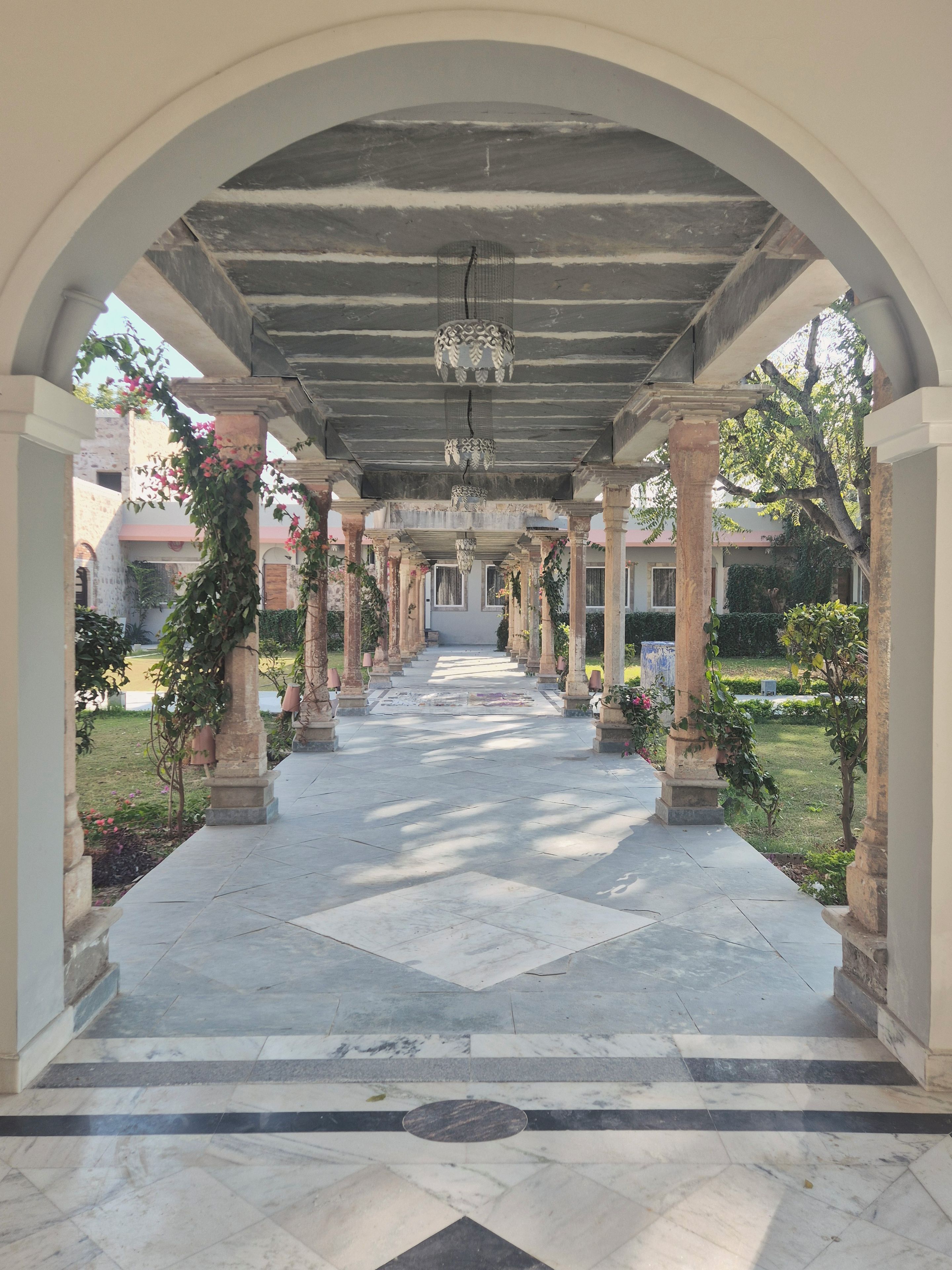A covered walkway with columns, a tiled floor, and hanging plants.