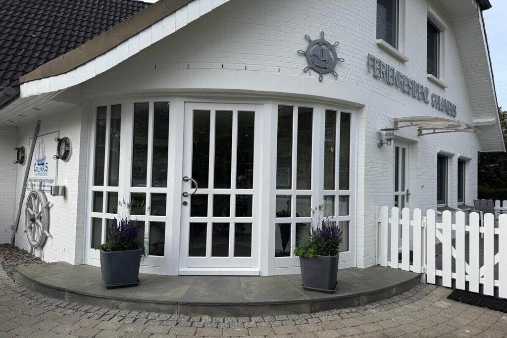Un edificio blanco con un letrero que dice 'FERIENRESIDENZ COMMERS' y una decoración con timón de barco.