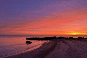 Ein Strand mit Sonnenuntergang, ruhigem Wasser und einer steinigen Küste.