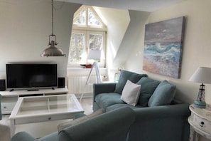 Ein Wohnzimmer mit Fernseher, einer Couch, einem Couchtisch und einem Gemälde an der Wand.