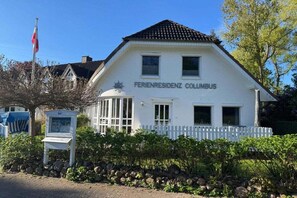 A white building with a sign reading 'FERIENRESIDENZ COLUMBUS' and a white picket fence in front. - Holiday apartment with 1 bedroom (Hohwacht)