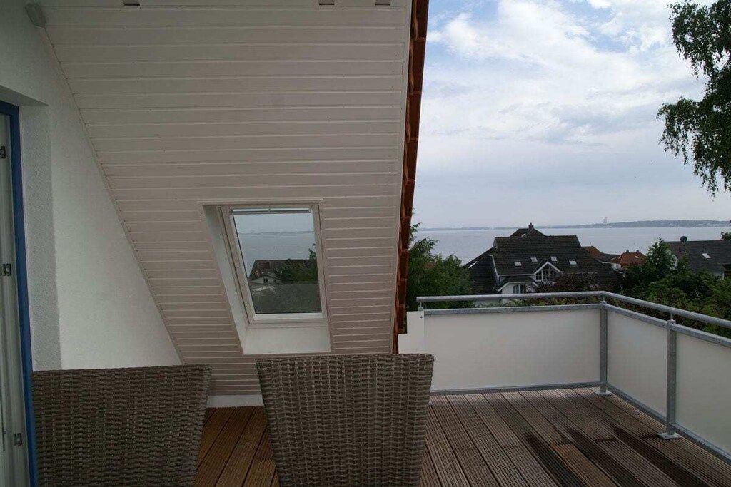 A balcony with a view of the sea, a window, and a chair.