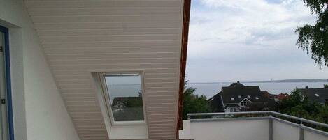 A balcony with a view of the sea, a window, and a chair.