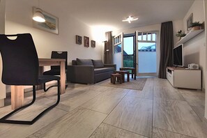 Ein modernes Wohnzimmer mit einer Couch, einem Esstisch mit Stühlen, einem Fernseher und einem Fenster mit Vorhängen.