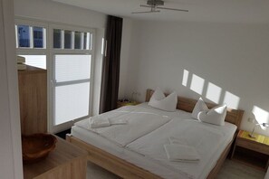 A double bed with white linens, a wooden headboard, and a bedside table with a lamp. - Holiday apartment with 1 bedroom (Zingst)