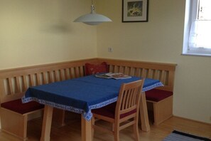 A dining area with a table covered by a blue tablecloth, wooden chairs with red cushions, and a wooden bench. - Holiday apartment in Söll with swimming pool (Söll)