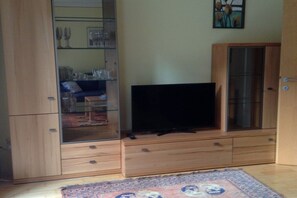 A room with a television on a wooden stand, a cabinet with glass doors, and a patterned rug on the floor. - Holiday apartment in Söll with swimming pool (Söll)