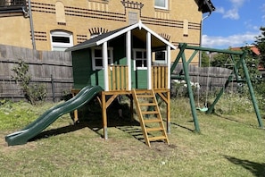 A children's playhouse with a slide and a swing set in a backyard. - Holiday home with 3 bedrooms (Friedrichsbrunn)