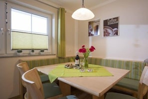 A dining area with a table, chairs, a bench, a hanging light fixture, and a window with blinds. - Holiday apartment with 2 bedrooms (Hippach)