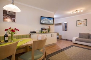 A dining area with a table set for two, a sofa, and a kitchen in the background. - Holiday apartment with 2 bedrooms (Hippach)