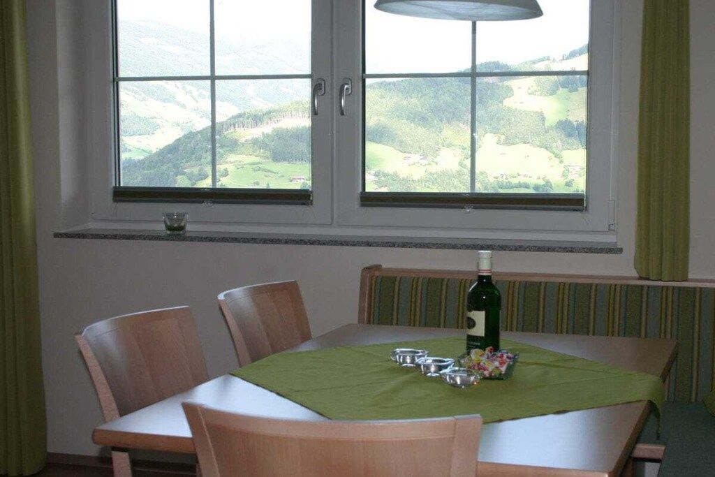 Un coin repas avec une table dressée pour quatre personnes, une bouteille de vin et une vue sur un paysage verdoyant par la fenêtre.