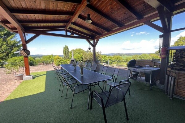 Une terrasse extérieure dotée d’un espace salon abrité, d’un barbecue et offrant une vue sur le paysage.