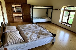 A room with a large bed, a bunk bed, wooden flooring, a window, and a door leading to another room. - ||---------------------Valahof Barn----------------------|| (Milevsko)