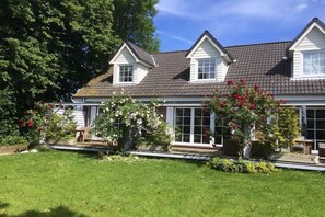 A two-story house with a sloped roof, large windows, and a well-maintained garden with flowering plants. - Holiday apartment in Nieby with swimming pool (Nieby)