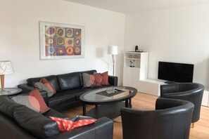 A modern living room with a black leather sofa, a glass coffee table, and a flat-screen TV. - on the inland lake in the town center (Heiligenhafen)