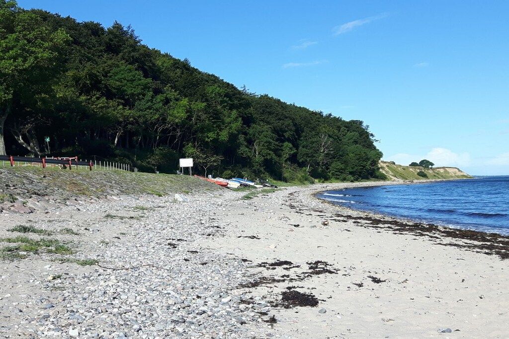 A beach with a rocky shoreline, a forested hill, and a clear sky.