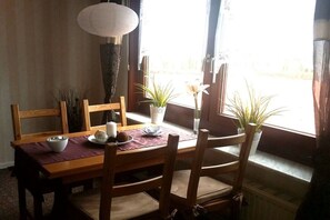 Ein Essbereich mit einem Holztisch, Stühlen, einer Blumenvase und einer stehenden Stehlampe.