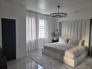 A modern bedroom with a large bed, a chandelier, and a view of the outdoors. - Royal Waterfront 5BR · Private Dock · Sleeps 16 (Port Charlotte)