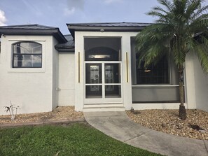 A building with a garage door, a window, and a palm tree. - Royal Waterfront 5BR · Private Dock · Sleeps 16 (Port Charlotte)