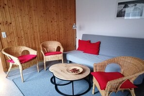 A room with a blue sofa, two wicker chairs with red cushions, a round wooden coffee table with a bowl of fruit, and a wooden wall. - ||--------------under the linden tree----------------|| (Quitzdorf\/ OT Steinölsa)
