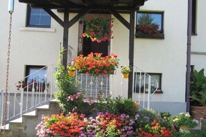 Un edificio con vestíbulo techado, una escalera y cestas de flores colgantes.