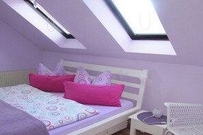Une chambre avec un puits de lumière, un lit avec une literie rose à motifs et une chaise blanche.