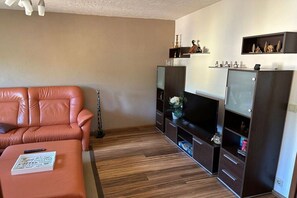 A living room with a leather sofa, a flat-screen TV, and built-in shelving with decorative items. - Holiday apartment with 2 bedrooms (Grünhain-Beierfeld)