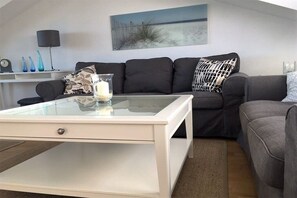 A modern living room with a glass-top coffee table, a grey sofa, and a painting on the wall. - Holiday home with 1 bedroom (Heiligenhafen)