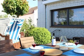 An outdoor patio with a table set for two, a striped beach chair, and a bottle of wine. - Holiday home with 1 bedroom (Heiligenhafen)