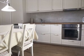 A kitchen with white cabinets, a wooden countertop, a stainless steel oven, and a hanging light fixture. - Holiday home with 1 bedroom (Heiligenhafen)