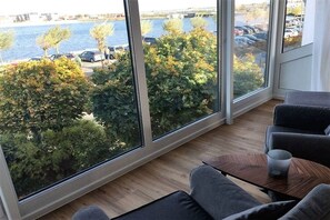 Een kamer met grote ramen, uitzicht op een rivier, en een zithoek met een tafel.