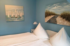 Une chambre à coucher avec un lit, deux oreillers, une table de chevet avec une lampe et deux tableaux accrochés au mur.