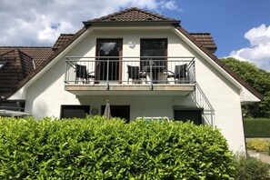 A two-story house with a balcony, a garage, and a well-maintained hedge in the foreground. - Holiday apartment with 2 bedrooms (Hohwacht)