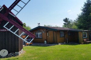 A wooden cabin with a sloped roof, a ladder, and a windmill structure to the left. - Summer log cabin "An de Möhl" (Ostseebad Dierhagen \/OT Dändorf)