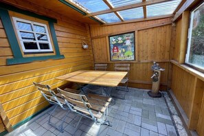 Une pièce en bois avec une table et des bancs, une fenêtre donnant sur un paysage agréable et un moulin à vent décoratif.