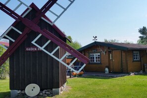 A traditional wooden windmill with a red and white structure, a small wooden building with a green roof in the background, and a clear sky. - Summer log cabin "An de Möhl" (Ostseebad Dierhagen \/OT Dändorf)