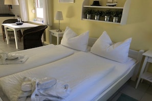 A hotel room with two beds, a desk, a chair, and a shelf with plants. - Holiday apartment with 1 bedroom (Hohwacht)
