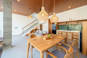 A modern kitchen with wooden cabinets, a built-in refrigerator, and a dining area with a wooden table and chairs. - Frankie's Villas (Klungkung)