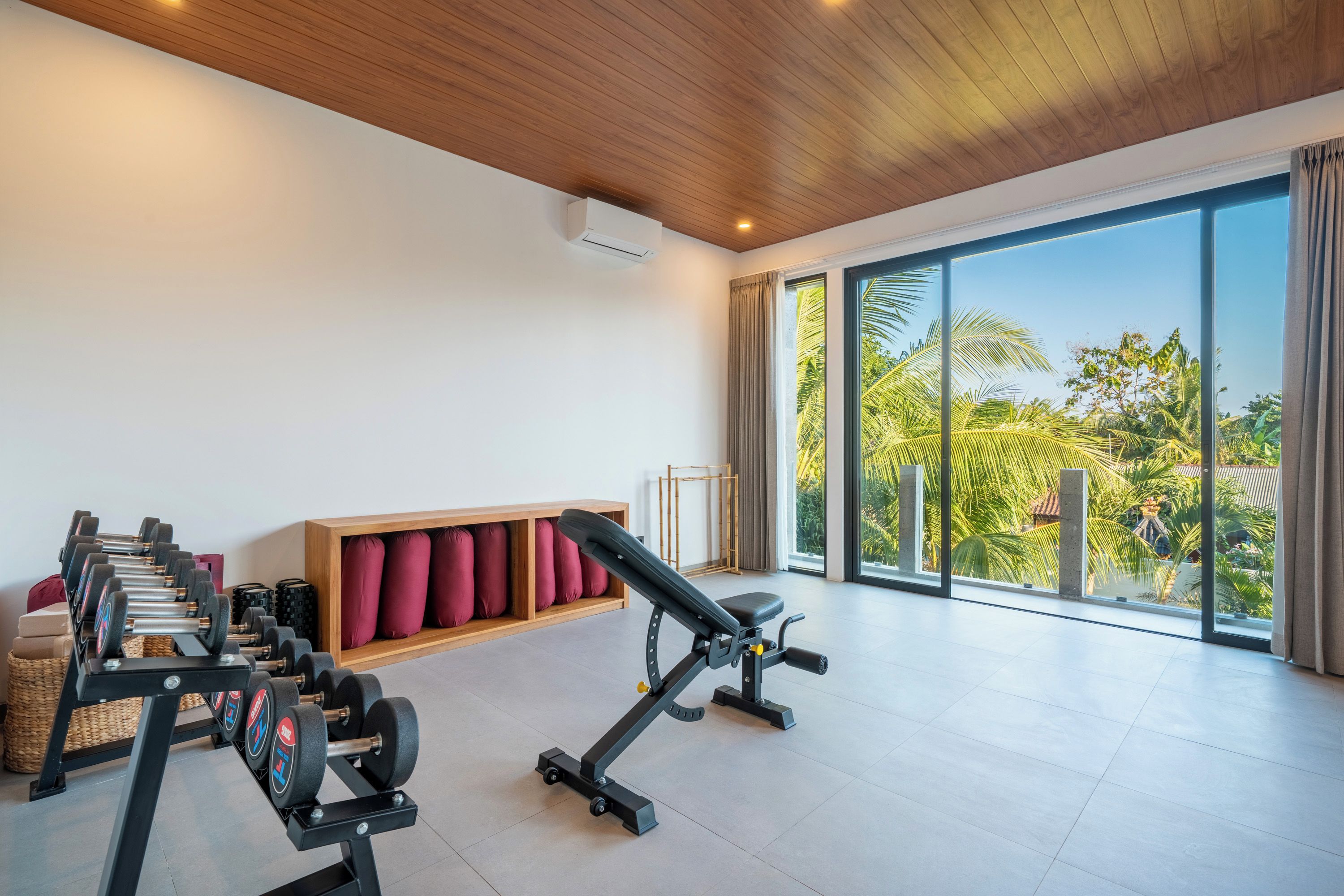 Un gimnasio con equipo de ejercicio, una banca y vistas a palmeras a través de amplios ventanales.