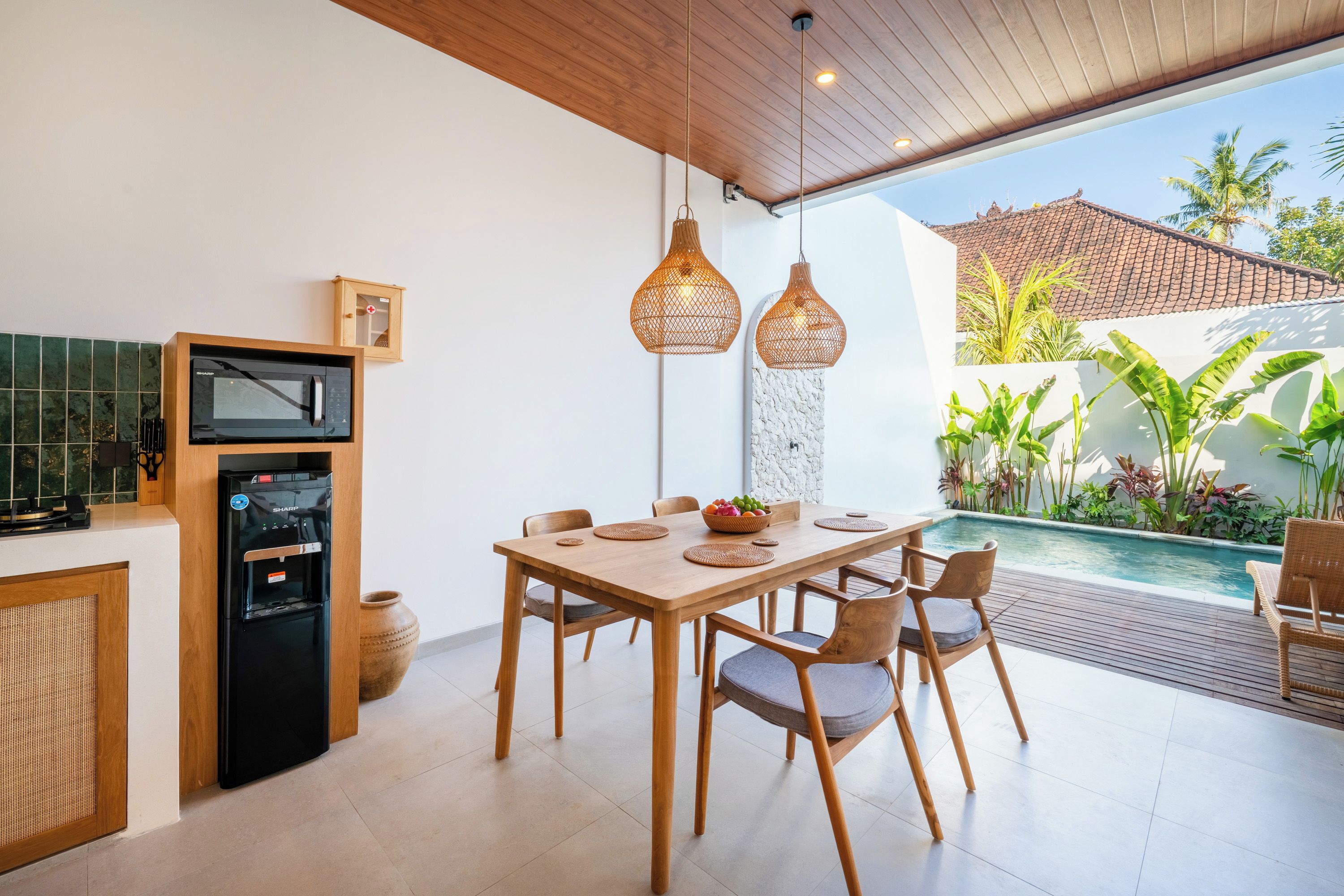 Cocina moderna con microondas integrado y dispensador de agua, un comedor con mesa y sillas de madera, y vistas a una piscina y jardín.