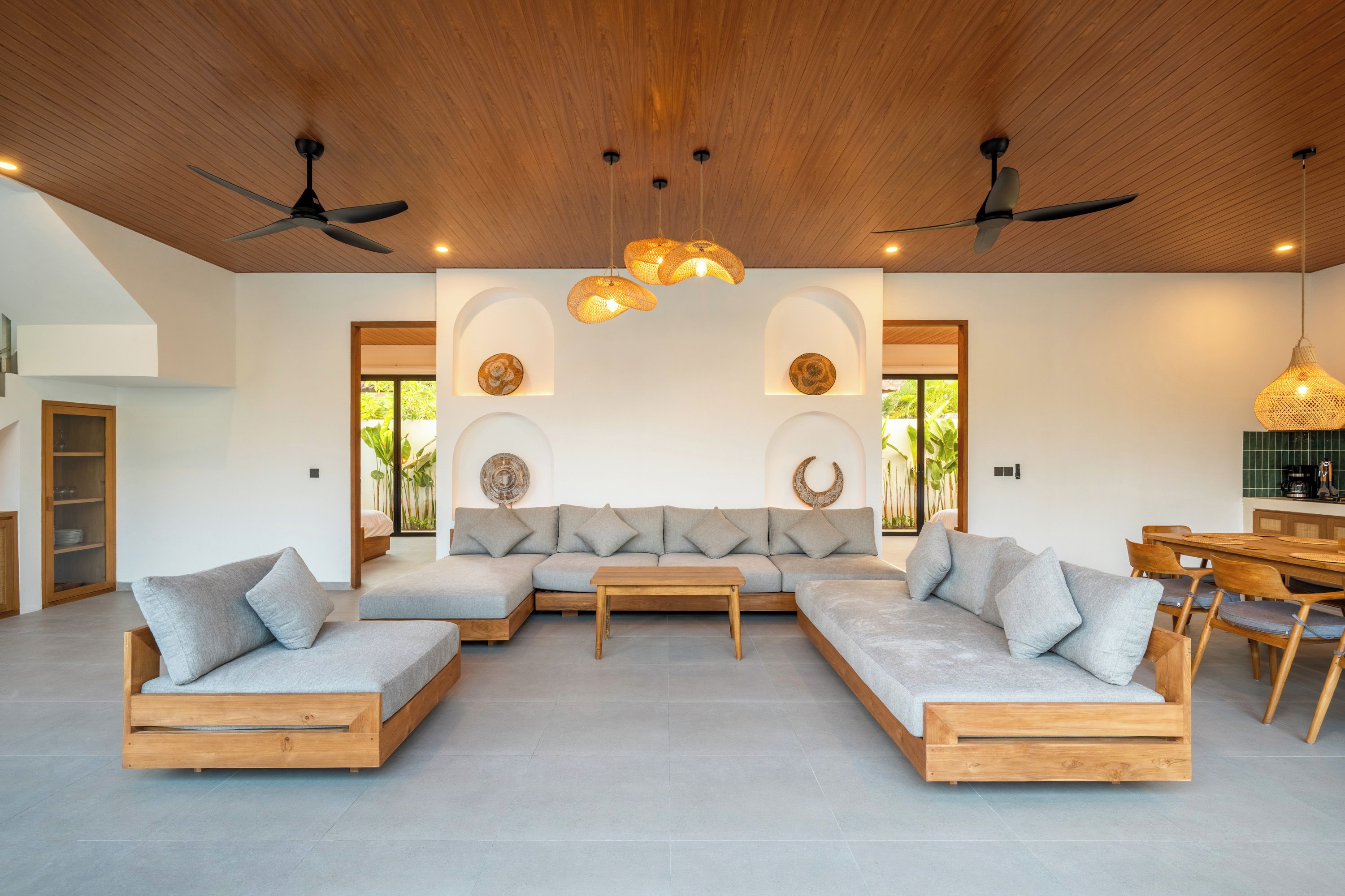 Una sala de estar moderna con un sofá seccional, piso de madera, ventiladores de techo y un comedor con una máquina de café.