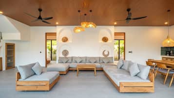 Una sala de estar moderna con un sofá seccional, piso de madera, ventiladores de techo y un comedor con una máquina de café.
