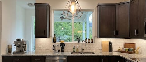 A modern kitchen with dark wood cabinets, a granite countertop, a built-in dishwasher, and a pendant light.