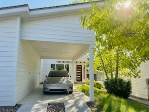 A modern house with a covered driveway, a car parked in the driveway, and a tree with green leaves.